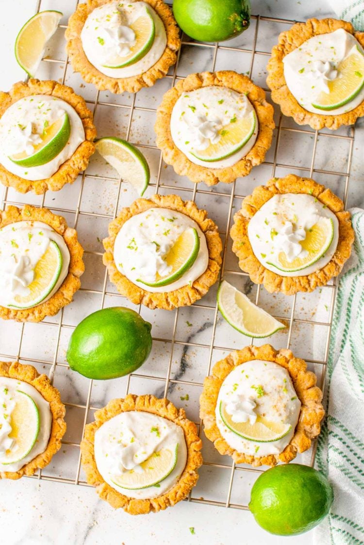 Overhead photo of key lime pie cookies on a wire rack with limes around them.