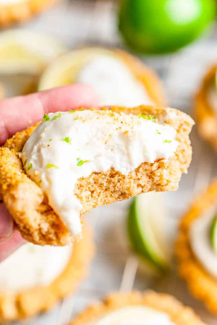 A woman's hand holding a key lime pie cookie with a bite taken out of it.