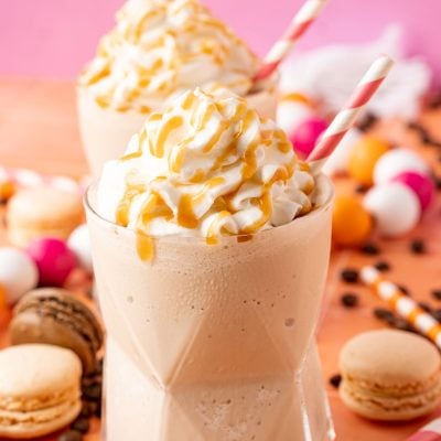 Two glasses of frozen coffee topped with whipped cream and caramel drizzle.