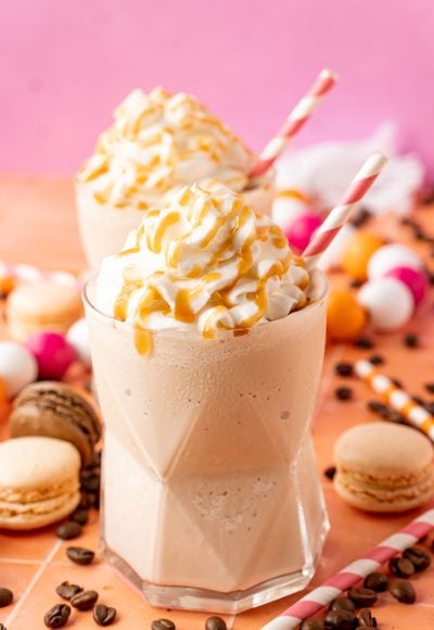 Two glasses of frozen coffee topped with whipped cream and caramel drizzle.