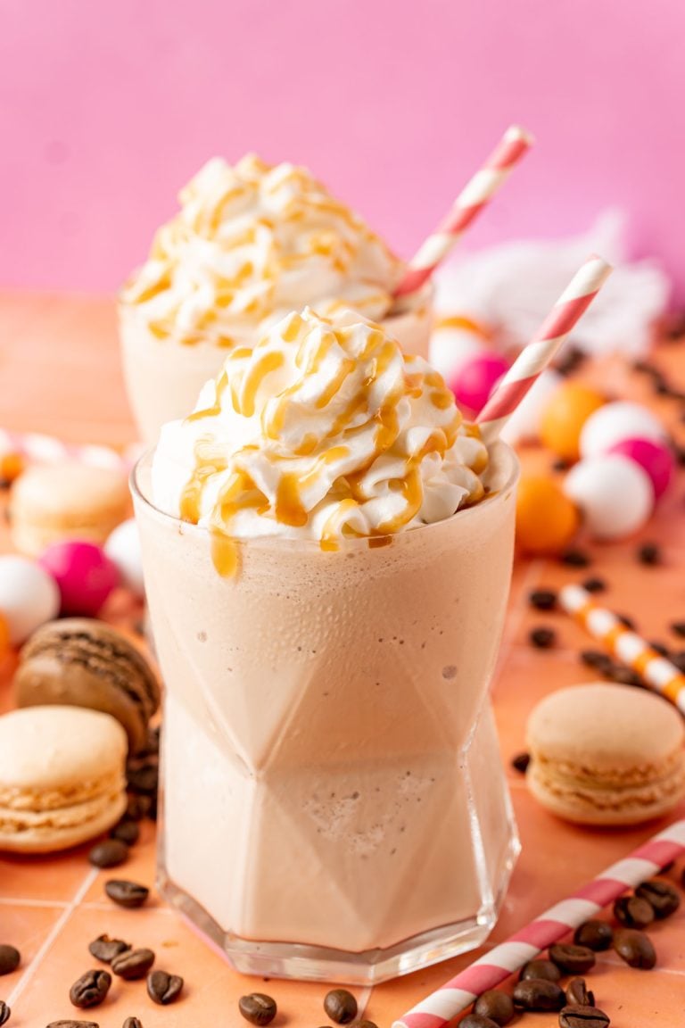 Two glasses of frozen coffee topped with whipped cream and caramel drizzle.