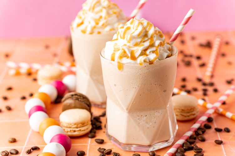 Two glasses of frozen coffee topped with whipped cream and caramel drizzle.