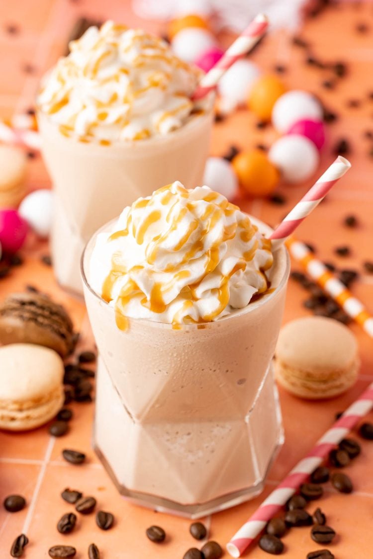 Two glasses of frozen coffee topped with whipped cream and caramel drizzle.