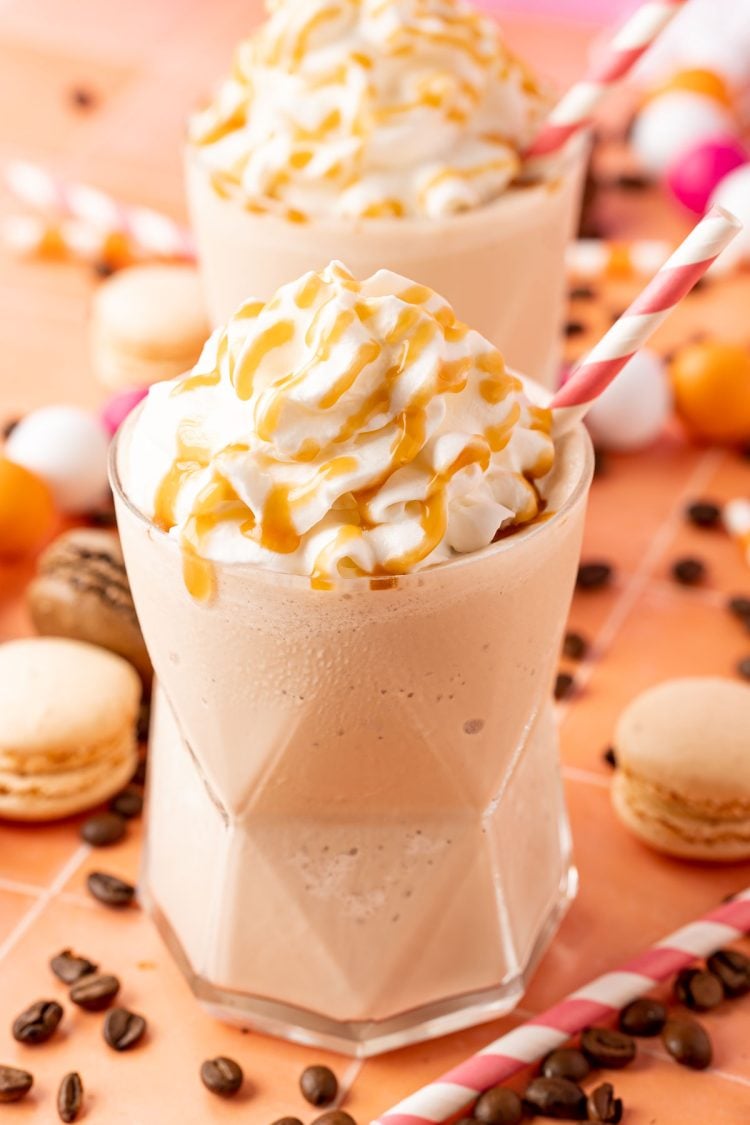 Two glasses of frozen coffee topped with whipped cream and caramel drizzle.