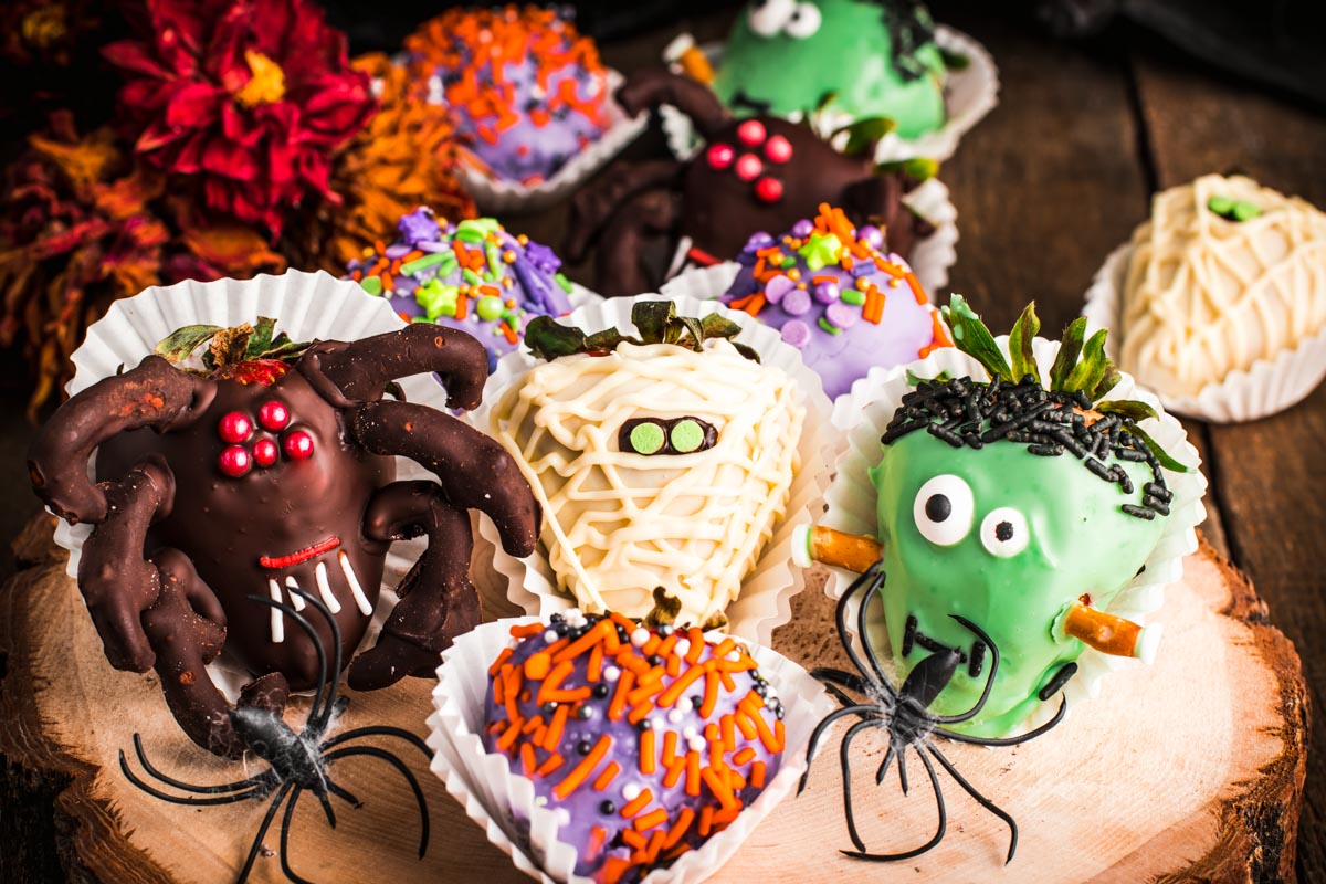 Halloween decorated strawberries on a wooden serving tray.