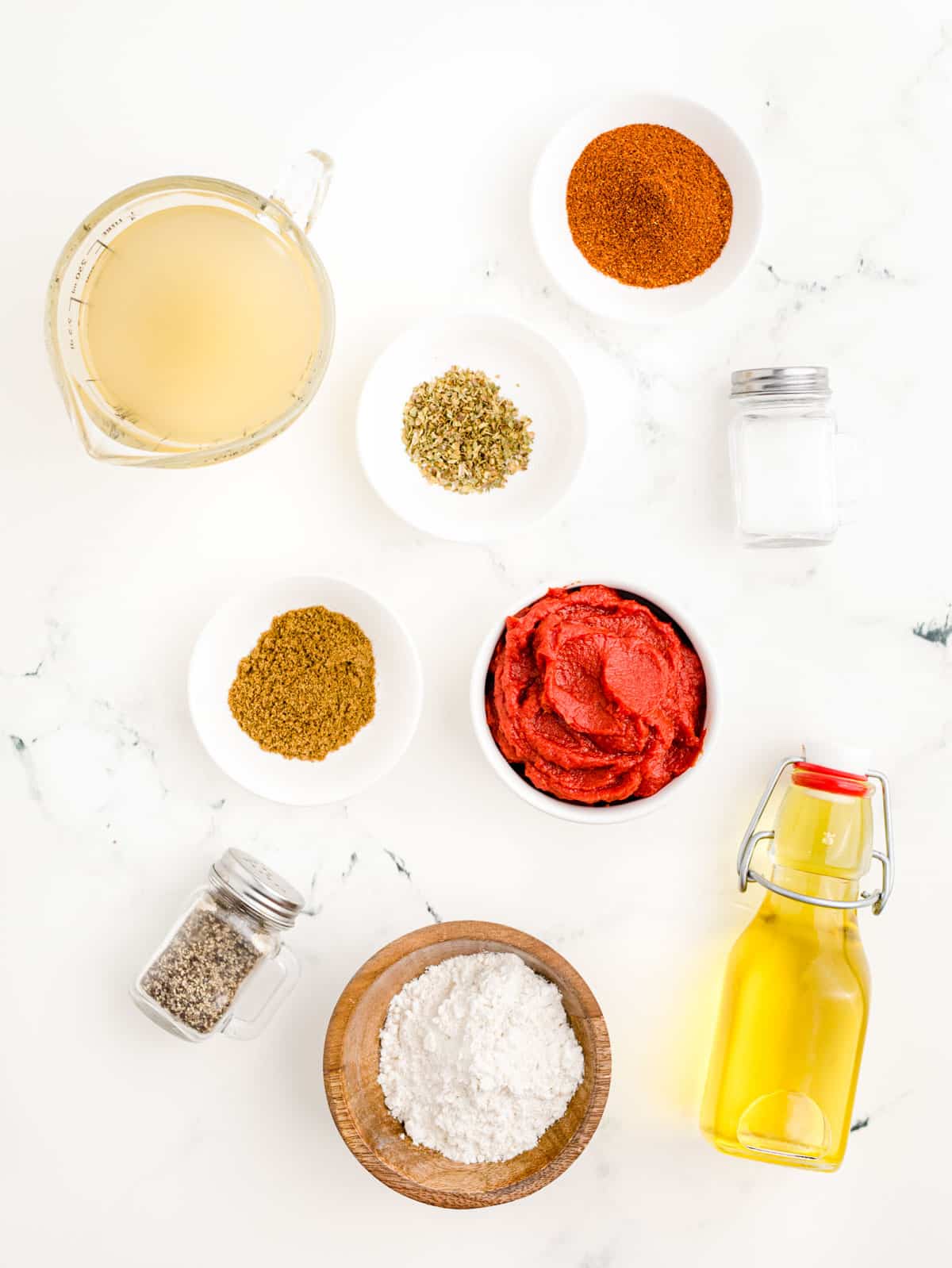 Ingredients to make enchilada sauce on a white marble counter.