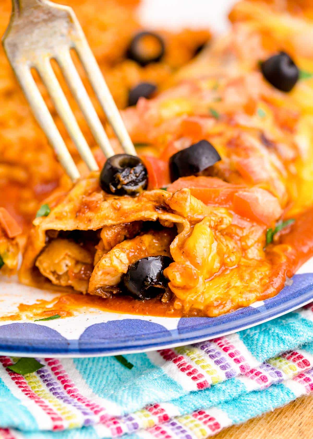 Chicken enchiladas covered in sauce and cheese with a fork taking a bite.