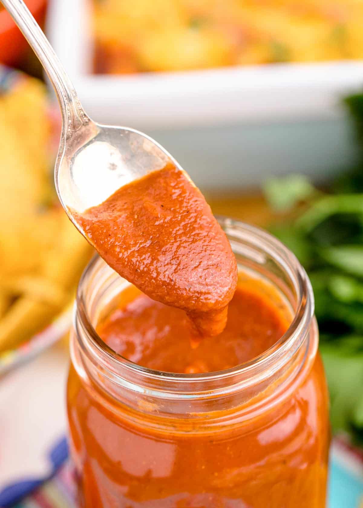 A spoon scooping enchilada sauce out of a jar.