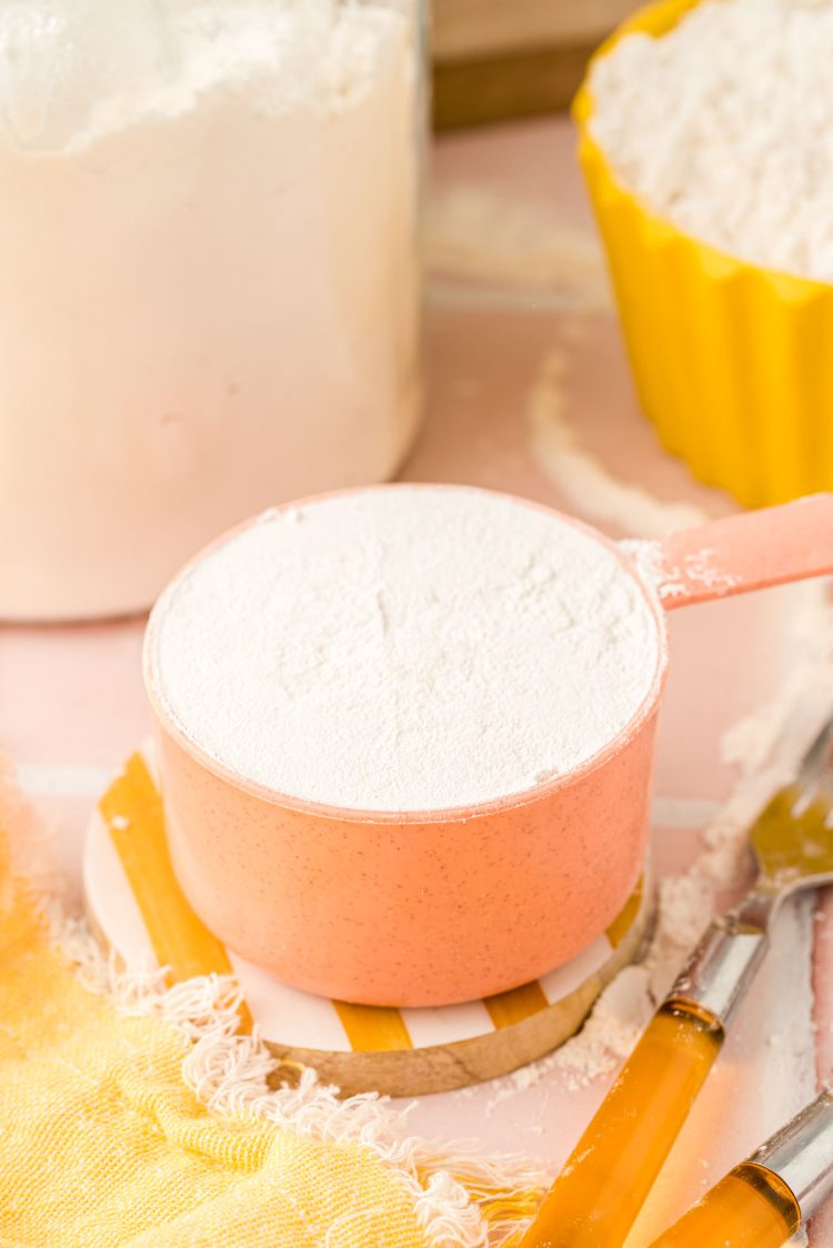 a peach colored measuring cup filled with flour.