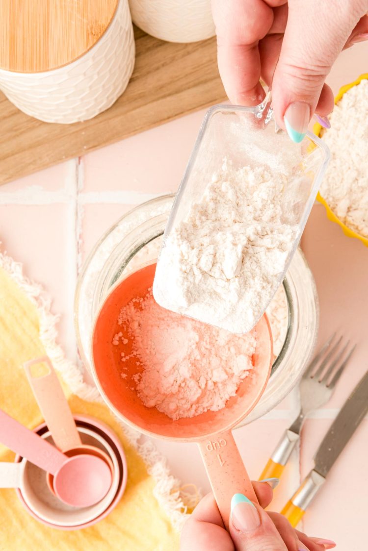 A scoop dumping flour into a measuring cup.