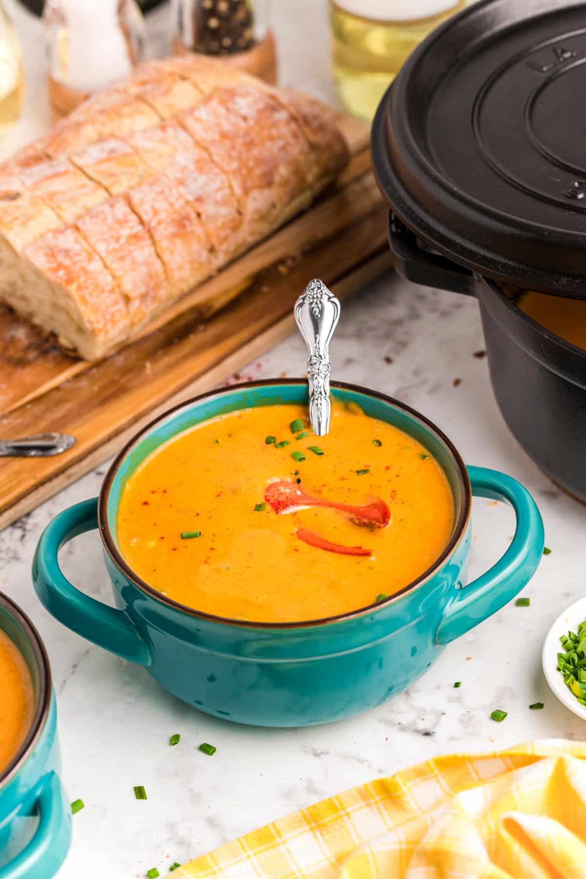 Lobster bisque in a teal serving bowl with bread in the background.