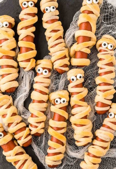 Mummy hot dogs on a black plate.