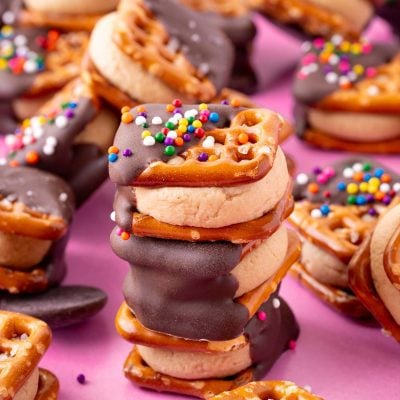 Three peanut butter pretzel bites stacked on a pink surface with more around it.