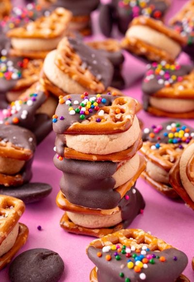 Three peanut butter pretzel bites stacked on a pink surface with more around it.