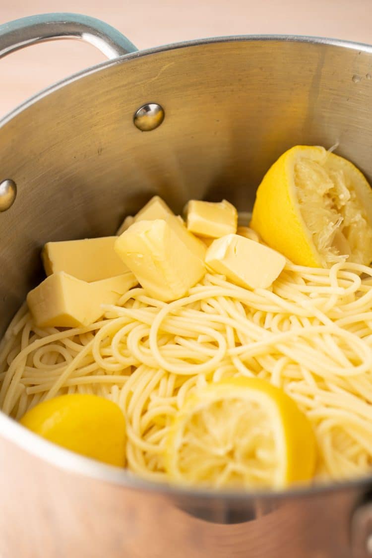 Spaghetti with lemon halves, lemon juice, and butter cubes in a stainless steel pot.