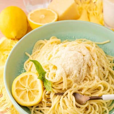 A green bowl filled with spaghetti limone on a yellow napkin.