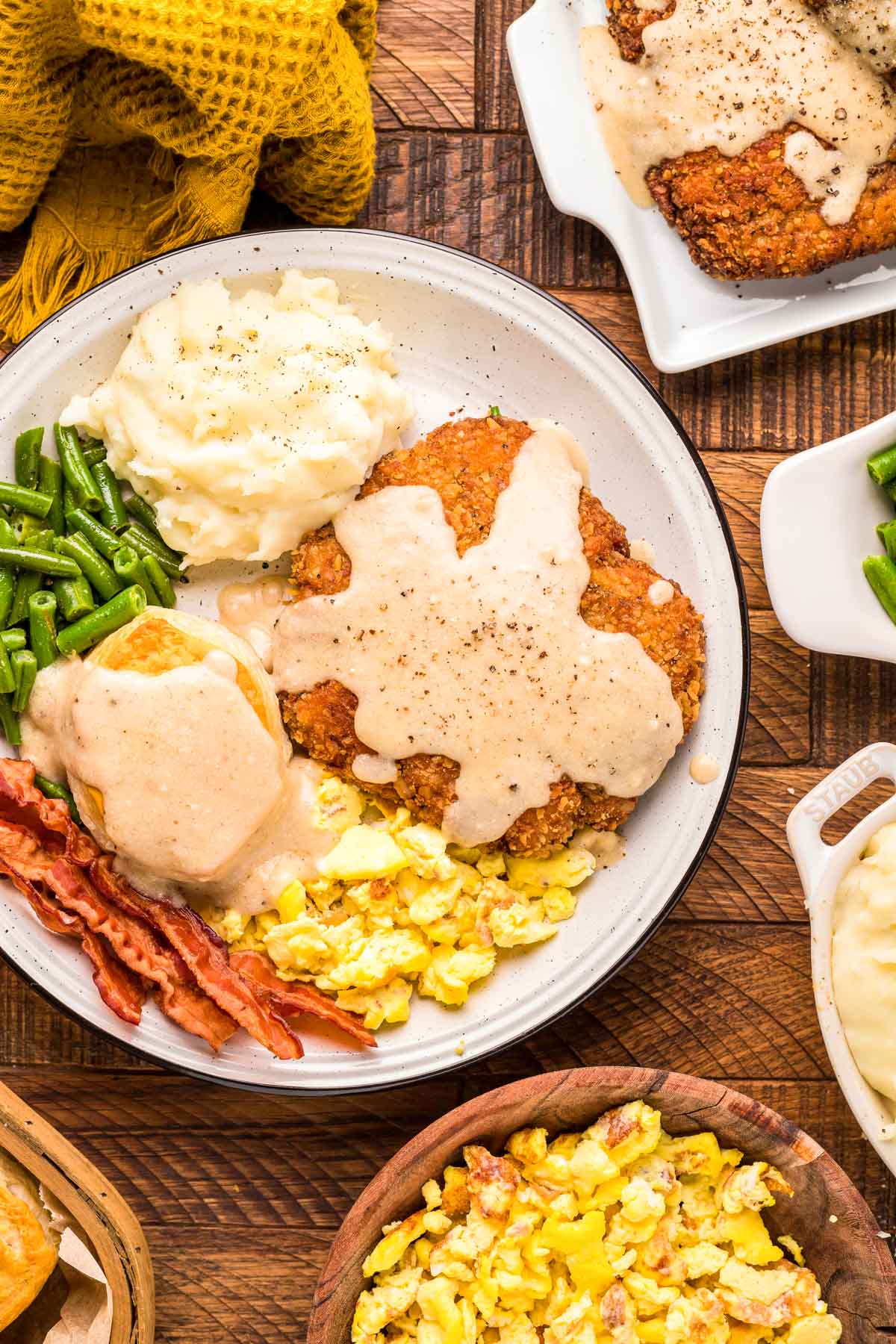 Overhead photo of a plate of country fried steak, bacon, eggs, and biscuits on a wooden table.