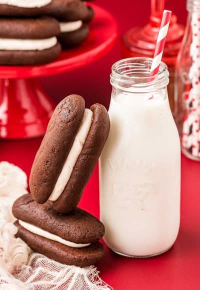 Homemade devil dogs on a red surface, on leaning against a glass milk bottle.