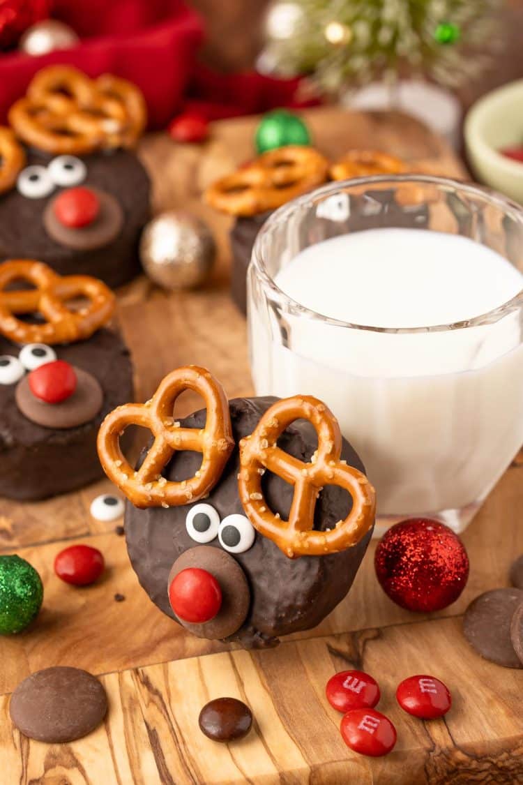 A mini reindeer cake leaning against a glass of milk.