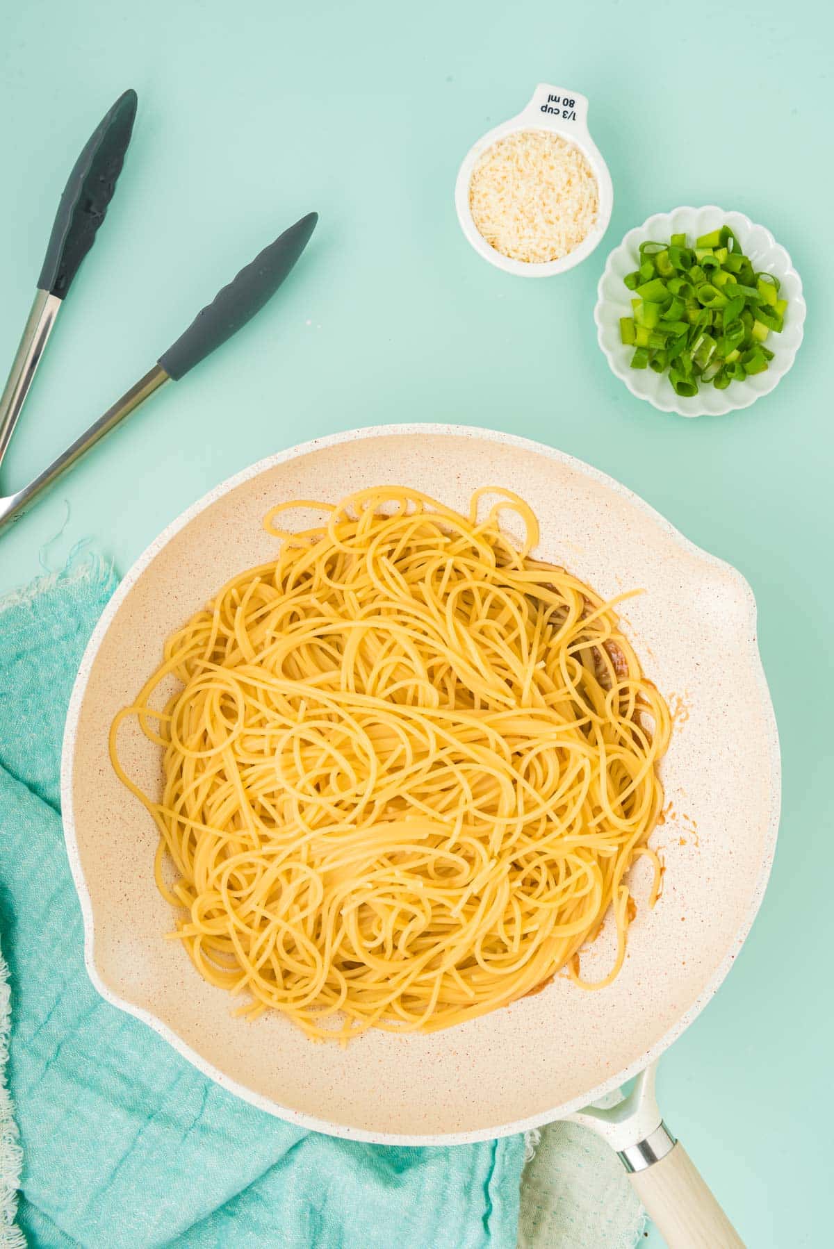 Spaghetti being added to garlic sauce in a wok.