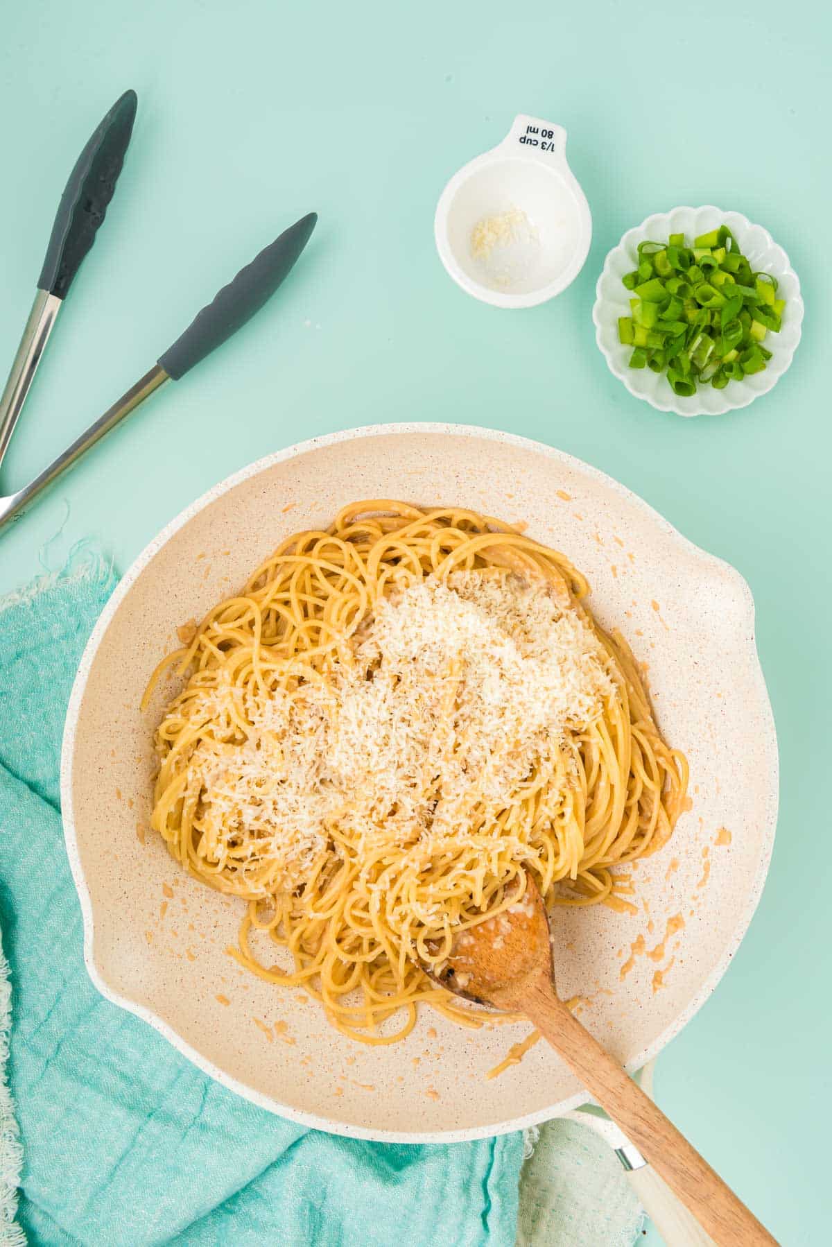 Spaghetti in a wok being mixed with other ingredients.