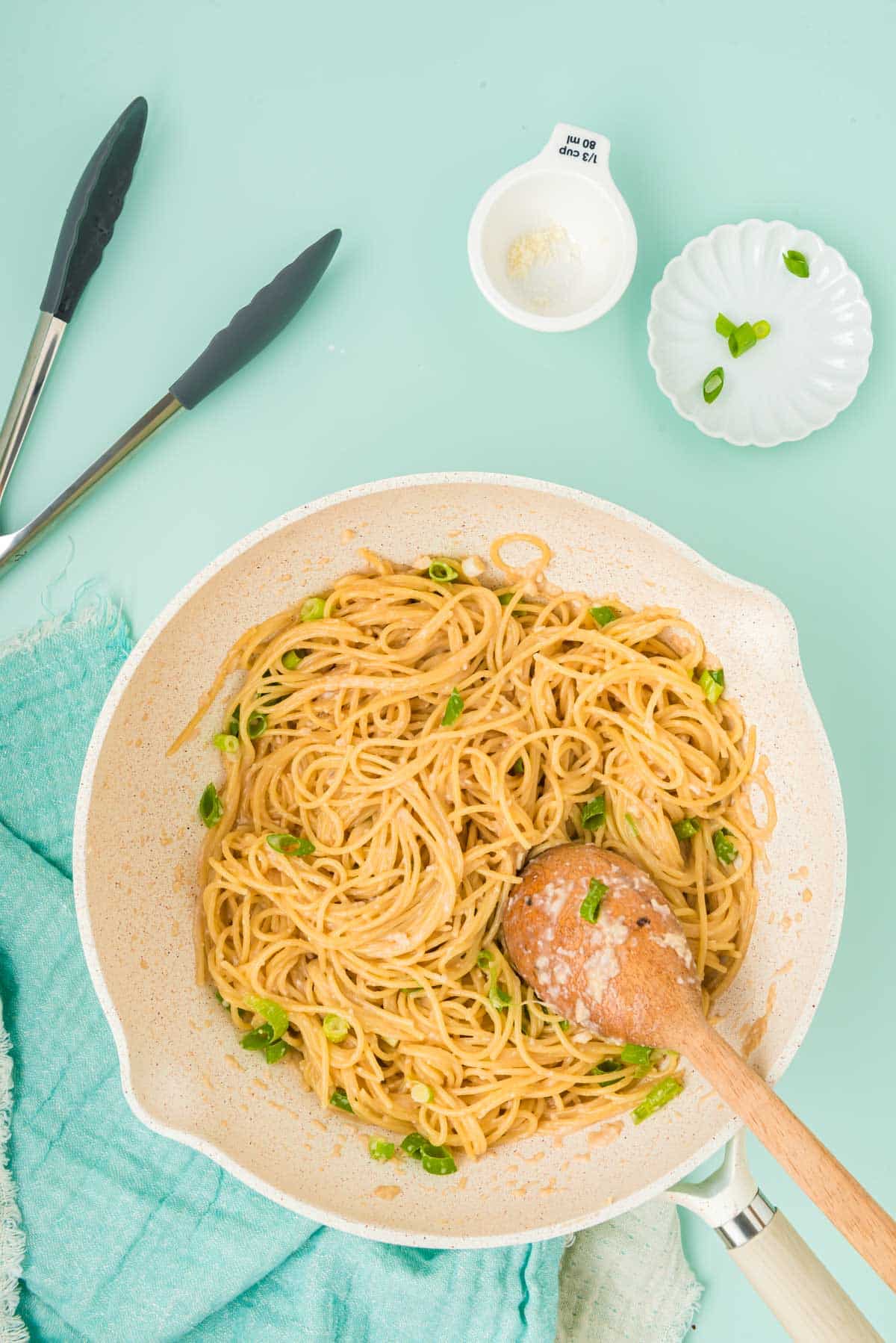Garlic noodles in a wok with a wooden spoon on a blue surface.