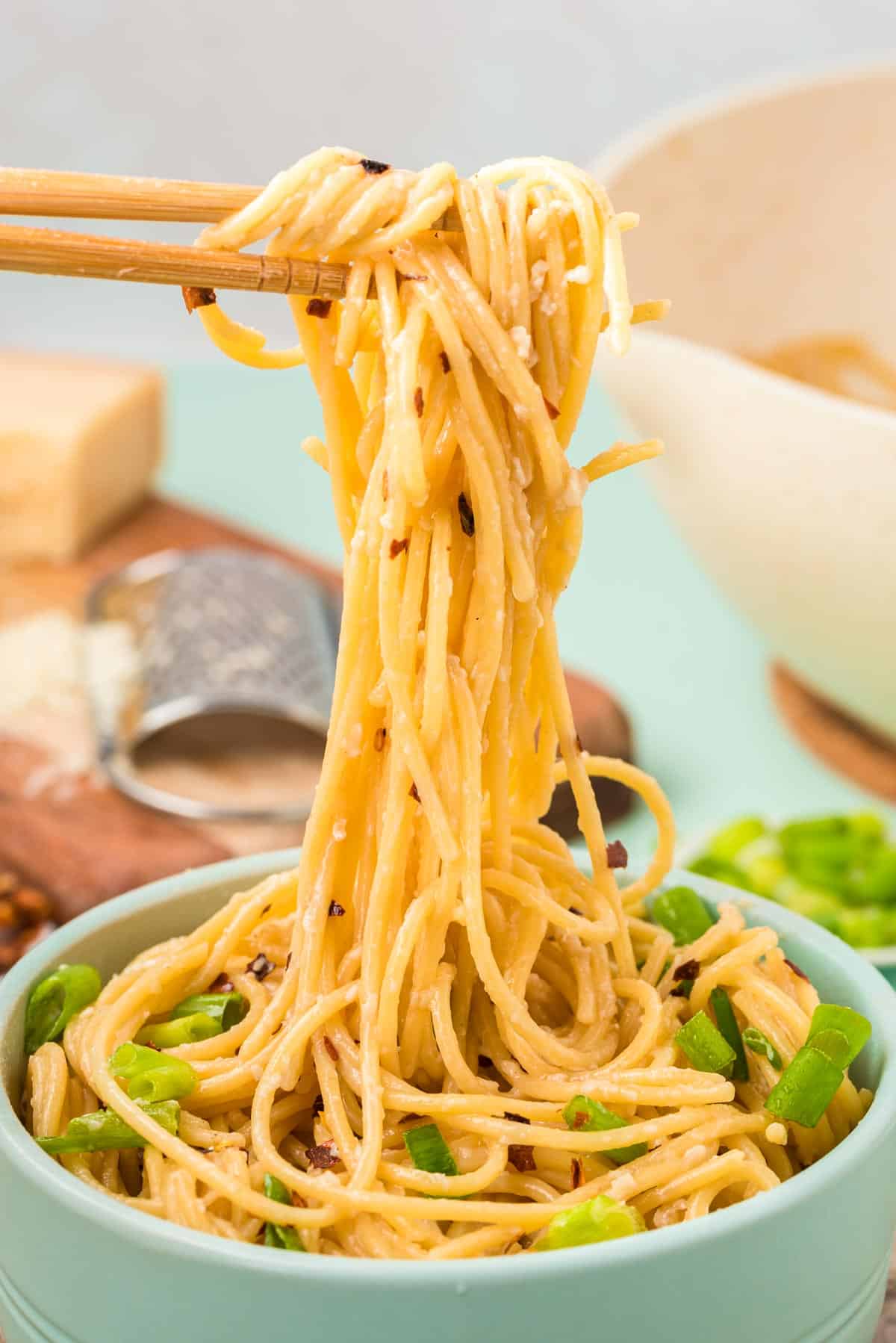 Chop sticks pulling garlic noodles out of a mint green bowl.