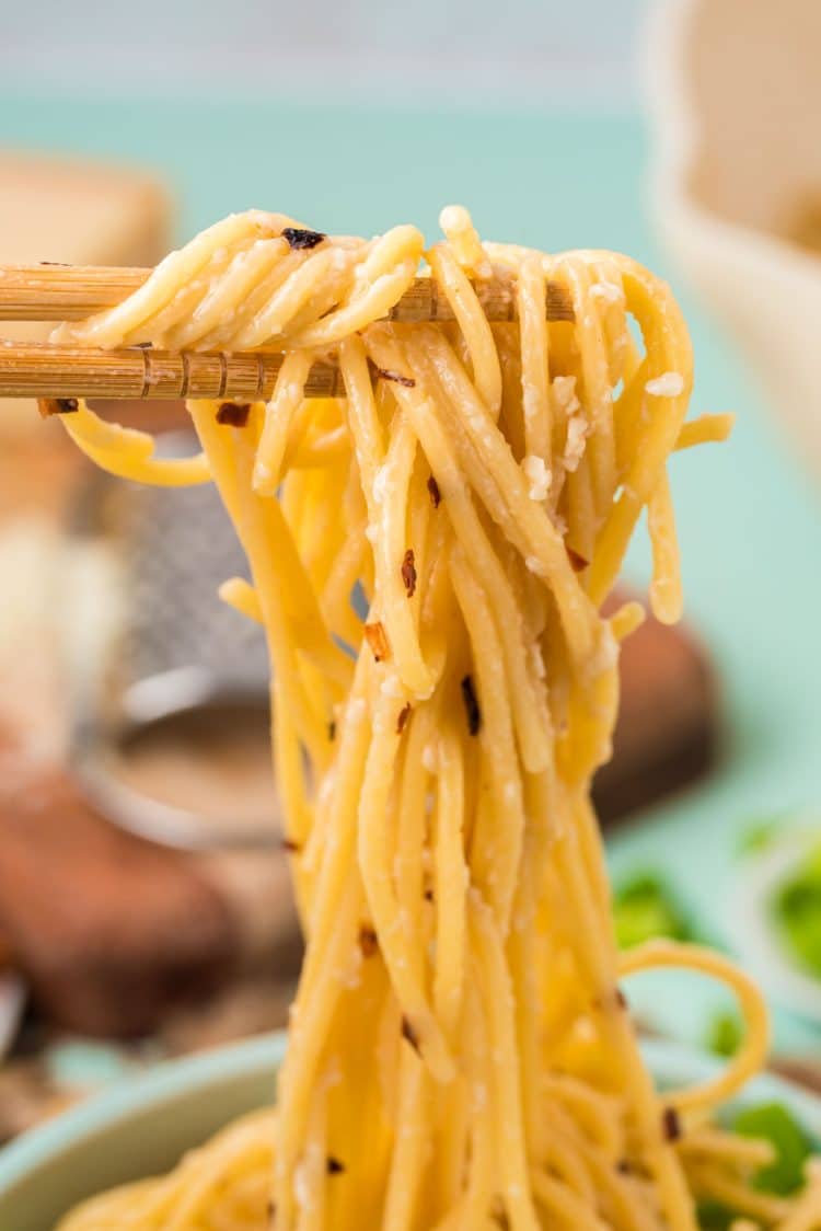 Close up of garlic noodles being pulled from a bowl with chopsticks.