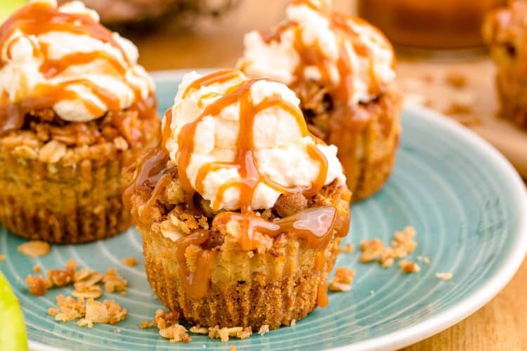 Mini caramel appl cheesecakes topped with whipped cream and caramel drizzle on a blue plate.