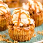 Mini caramel appl cheesecakes topped with whipped cream and caramel drizzle on a blue plate.