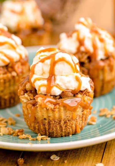 Mini caramel appl cheesecakes topped with whipped cream and caramel drizzle on a blue plate.