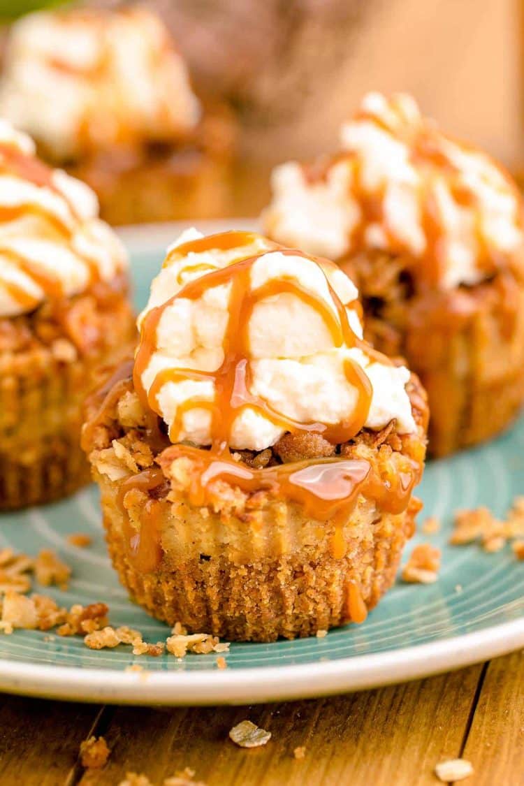 Mini caramel appl cheesecakes topped with whipped cream and caramel drizzle on a blue plate.