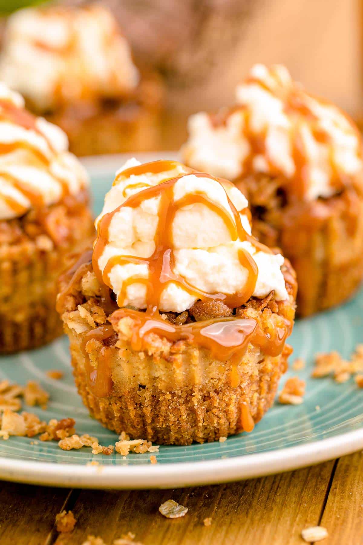 Mini caramel appl cheesecakes topped with whipped cream and caramel drizzle on a blue plate.