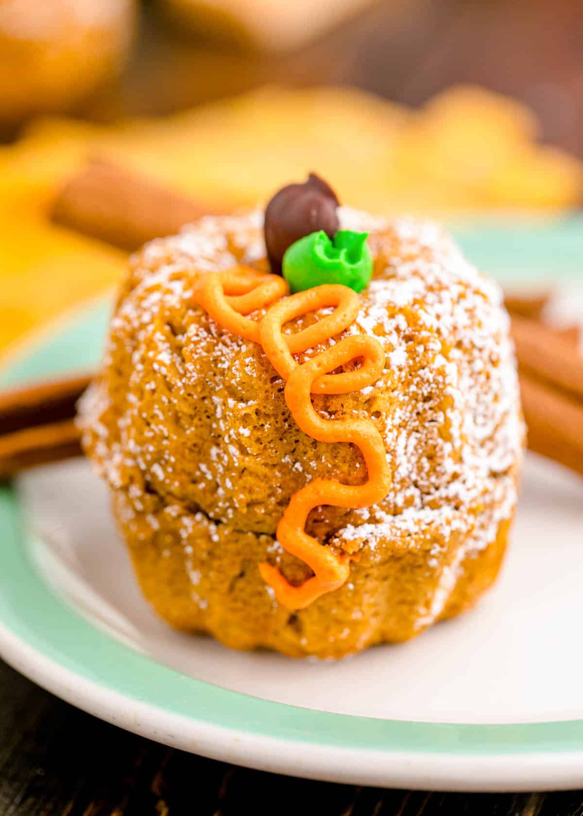 A mini pumpkin bundt cake on a white and mint green plate.