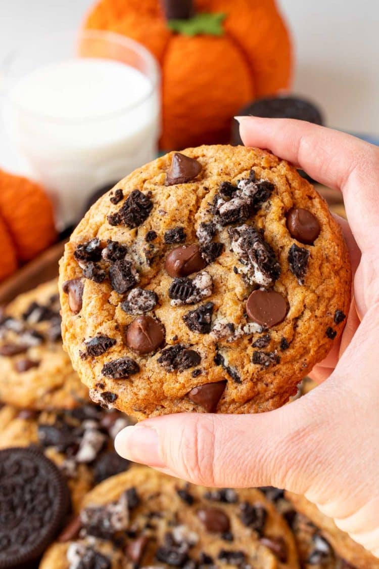 A woman's hand holding a big Oreo pumpkin chocolate chip cookie to the camera.