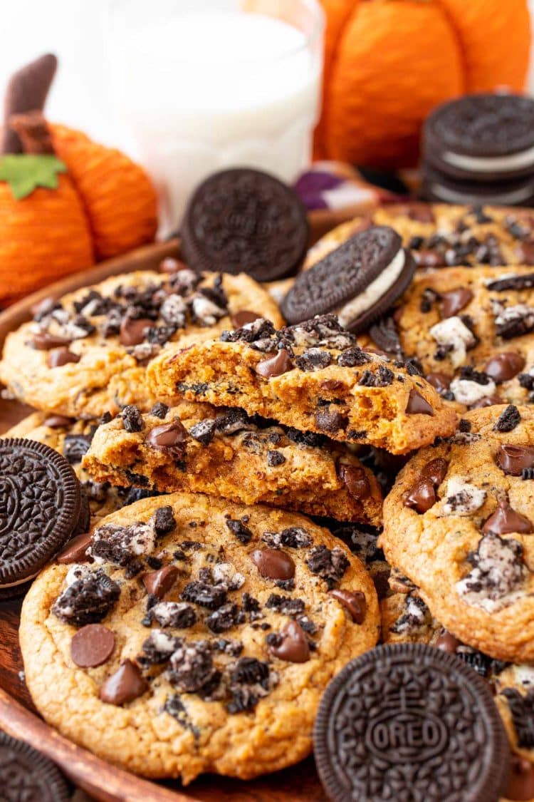 Oreo Pumpkin chocolate chip cookies piled on a plate, the top one is broken in half.