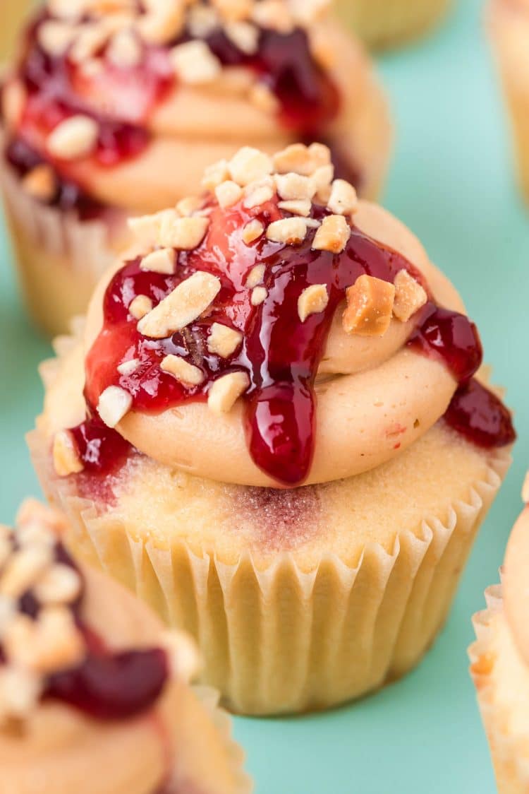 Peanut butter jelly cupcake on a blue surface surrounded by more cupcakes.