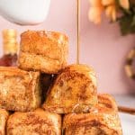 A stack of slider french toast on a white plate with syrup being poured over the top.