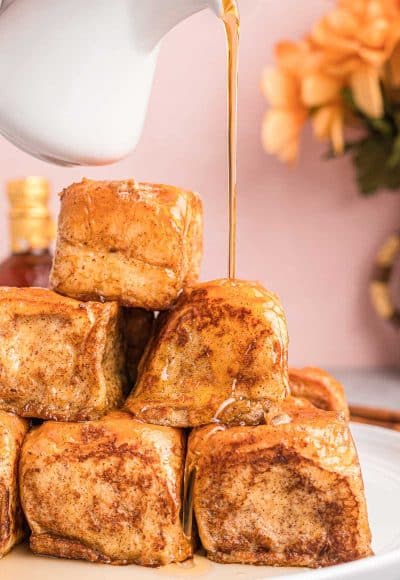 A stack of slider french toast on a white plate with syrup being poured over the top.