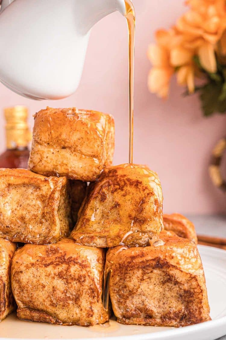 A stack of slider french toast on a white plate with syrup being poured over the top.