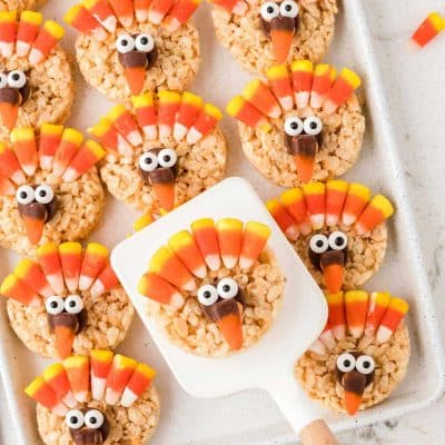 Rice Krispie treats decorated as turkeys on a sheet pan with a spatula lifting one away.