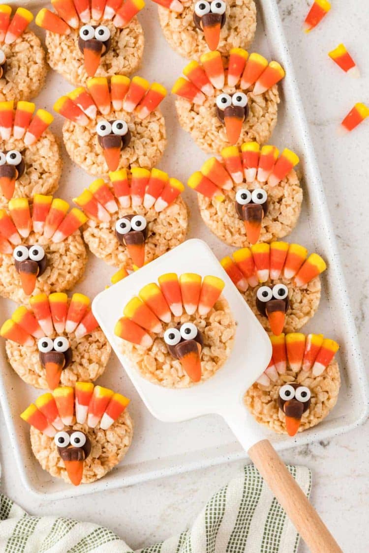 Rice Krispie treats decorated as turkeys on a sheet pan with a spatula lifting one away.