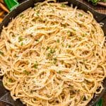 Overhead photo of bucatini cacio e pepe in a green and black skillet on a wooden table.