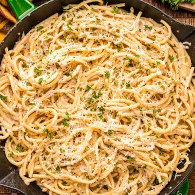 Overhead photo of bucatini cacio e pepe in a green and black skillet on a wooden table.