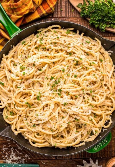 Overhead photo of bucatini cacio e pepe in a green and black skillet on a wooden table.