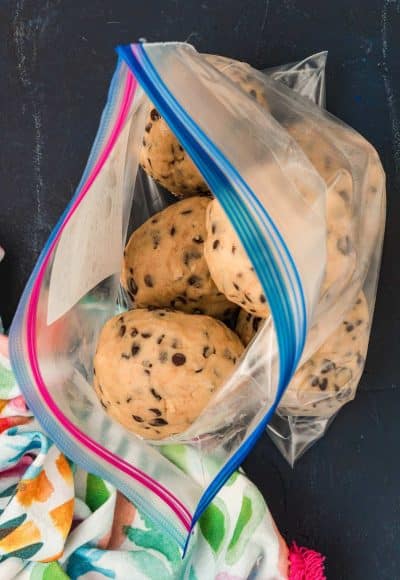 Balls of frozen cookie dough being added to a large ziploc bag.