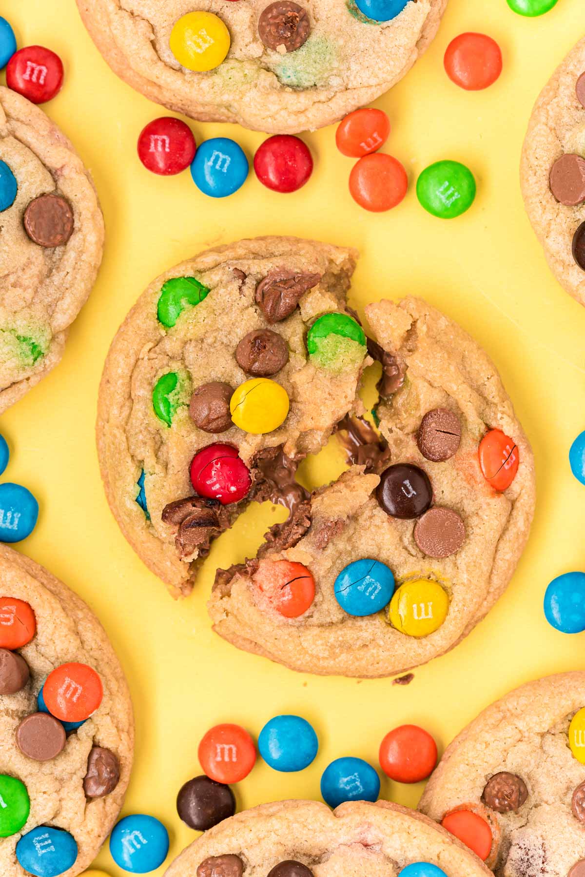 M&M cookies on a yellow surface the middle one has been broken in half.