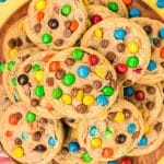 m&m cookies stacked on a wooden plate.