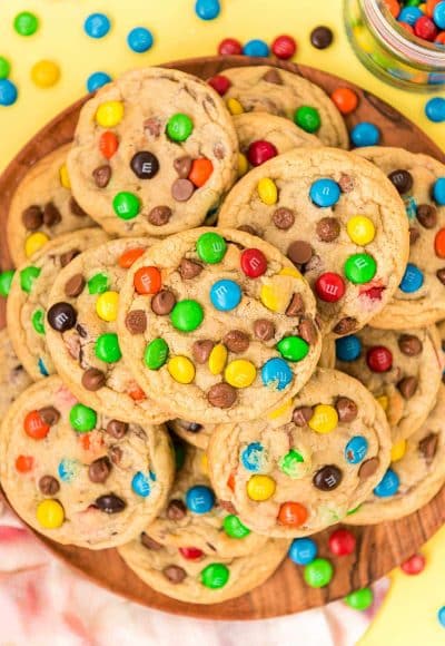 m&m cookies stacked on a wooden plate.