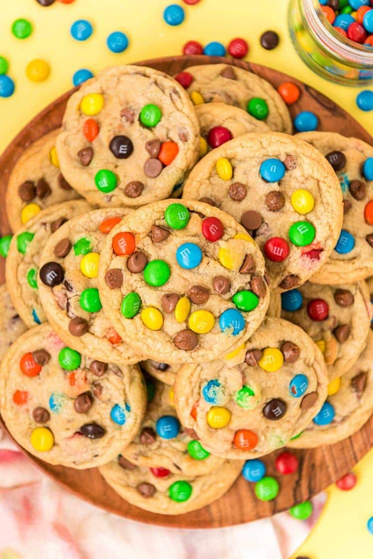 m&m cookies stacked on a wooden plate.